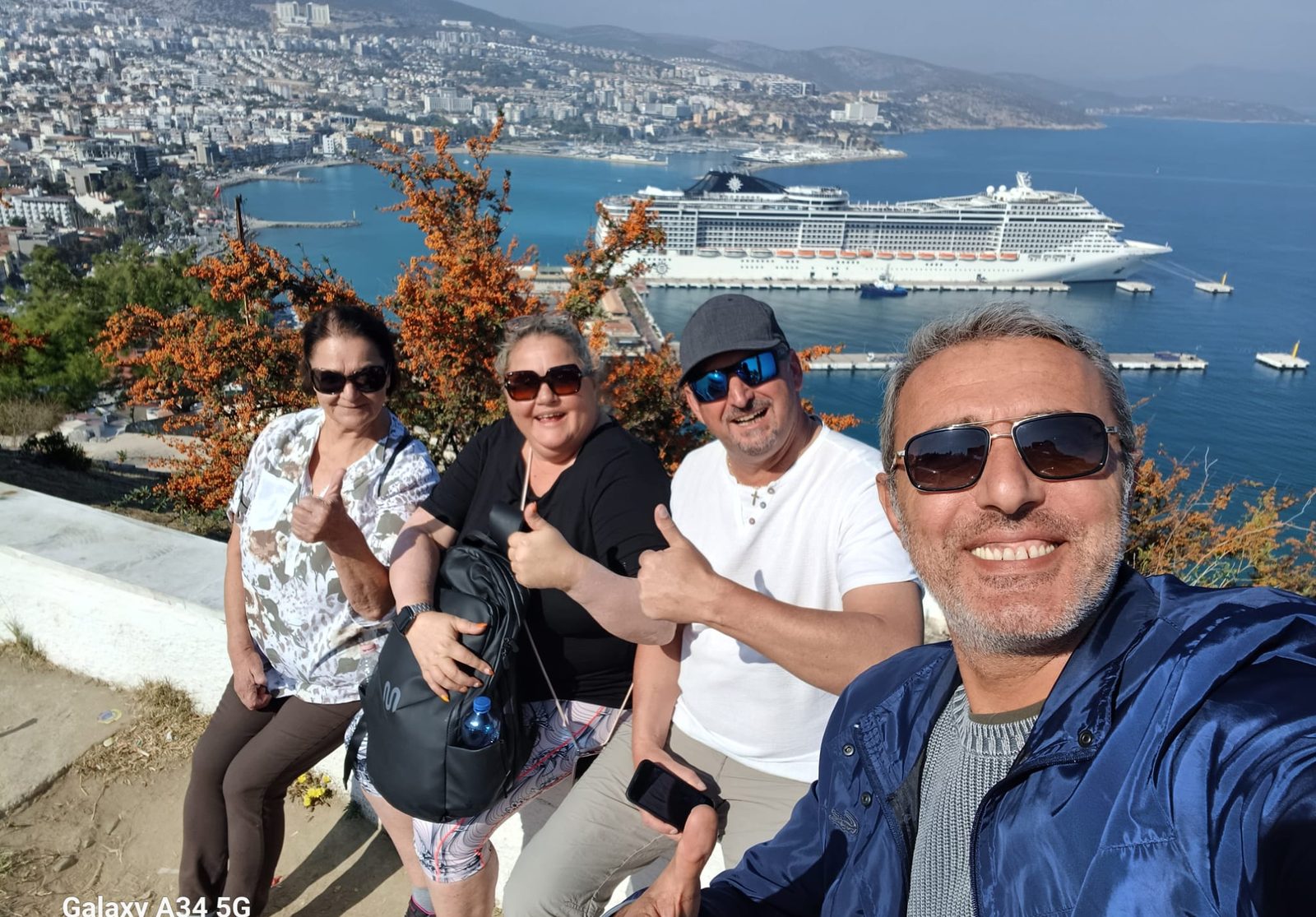 Akın with smiling guests on the hill above Kusadasi cruise port, their ship in the bay behind them